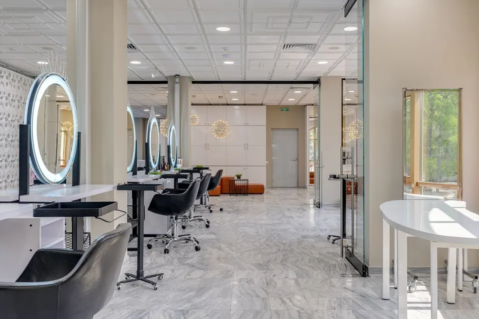 A bright salon floor with a row of styling stations and ring-lit mirrors