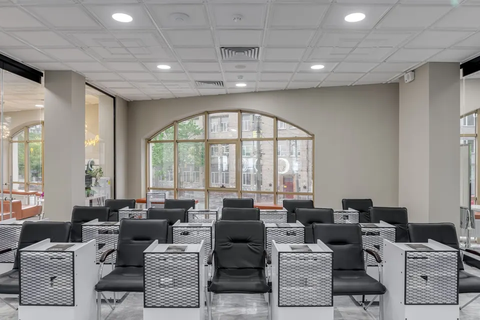 A bright salon floor with rows of white manicure tables under arched windows